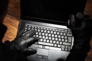 Burglar holding a torch stealing data from a laptop concept for computer security, corporate or identity theft